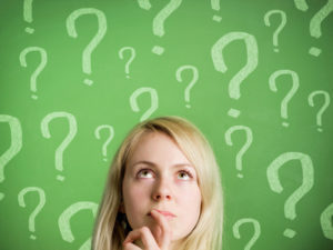 Thinking woman in front of blackboard with question marks